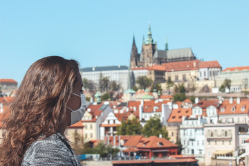 Young woman with medical face mask on Charles Bridge in Prague, Czech Republic. Blurred old town...