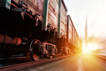 Freight train passing at sunset. Train carrying cargo under the rays of the setting sun.