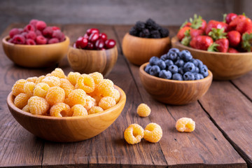 Yellow and red raspberries and other berries in bowls on a dark wooden background.