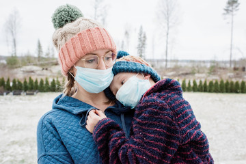 mother carrying son with face masks on as protection from virus & flu