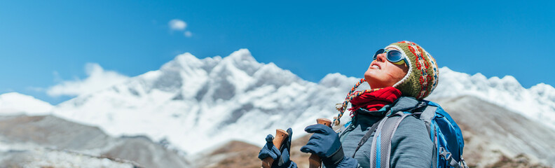 Young hiker backpacker female taking brake in hike walking during high altitude Everest Base Camp (EBC) route with snow Himalayan peaks on background.She using trekking poles. Active vacations concept - obrazy, fototapety, plakaty