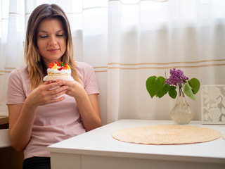 Woman in pink t-shirt sitting at a white table and trying to say no to junk food