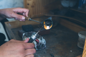 Detail of hands using blowtorch to melt fine metal while crafting