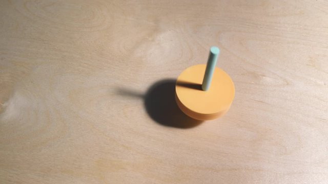 Spinning Top 3D printed in Orange and Minty plactic spinning over a plywood table.