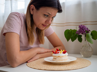 Woman in pink t-shirt sitting at a white table and trying to say no to junk food