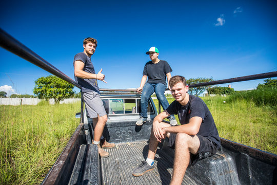 Three young men ride through field in back of 4x4 truck.