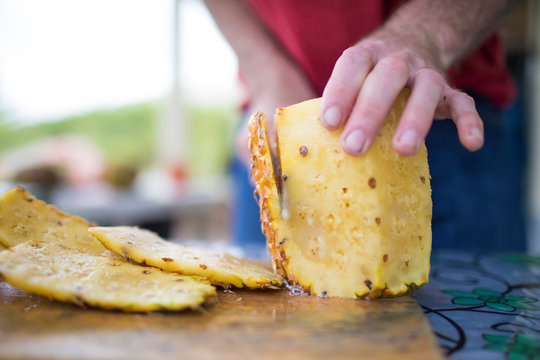 Detailed view of man slicing fresh pineapple outdoors