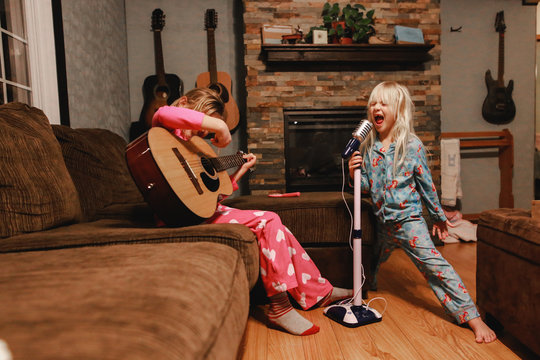 Naklejki Young girls singing loudly and playing guitar in living room