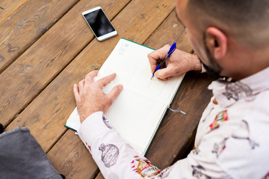 Young bearded businessman sitting at table, making notes in notebook