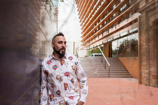 Bearded male with hand on pocket leaning on wall, looking camera