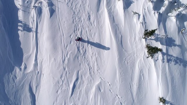 Top aerial view Footage: a girl in bright ski equipment is walking along the valley and then stopping waving her hands. snow-covered field with snowstorm inflators. winter outdoor activity. 4k