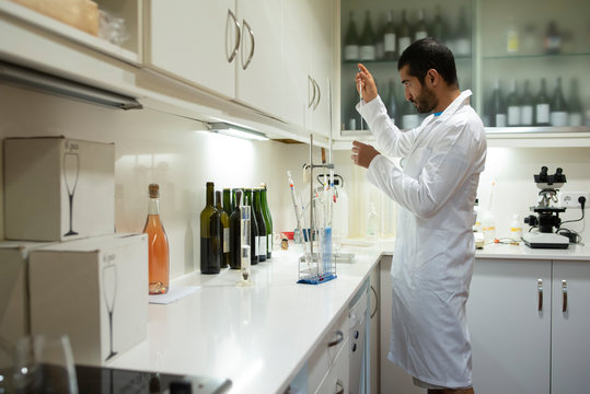 Arabic winemaker working in winelab wearing white gown and gloves.