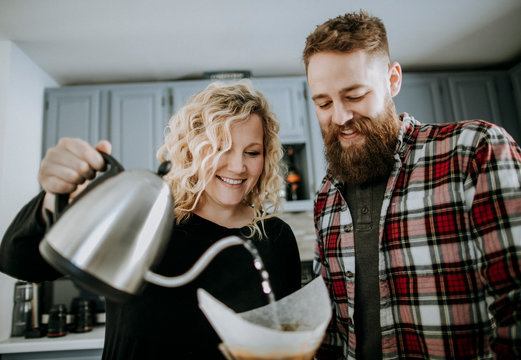 smiling young couple makes pour over coffee in their kitchen