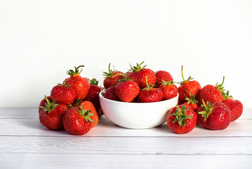 Heap of fresh strawberries in white ceramic bowl on rustic white wooden background