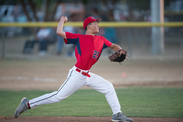 teen baseball player pitcher in red uniform in full wind up on the mound