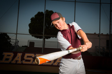 Portrait of a High School baseball player in maroon uniform swing his bat
