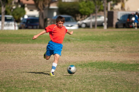 Young soccer player in red blue uniform kicking soccer ball in park
