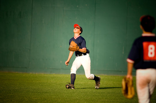 young baseball player in sunglasses looking up at a fly ball