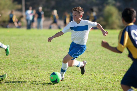 Fototapeta Teen soccer player dribbling ball through defenders