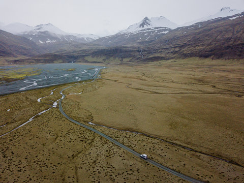 Aerial of car driving down gravel road in mountain valley in eas