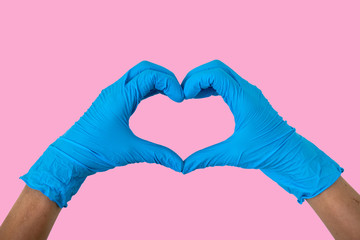 Obraz premium Human rising hands make finger heart shape wearing blue disposable latex glove, rubber glove for professional medical safety and hygiene protection from Coronavirus disease COVID-19 - Pink background