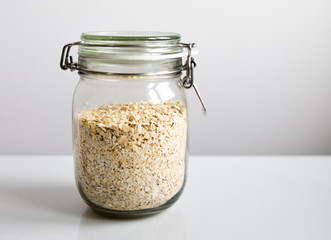 Close view of a glass jar filled with oatmeal flakes and a white background with copy space