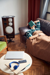 Tire young man with book on face sleeping on sofa