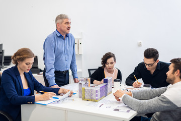 A team of construction designers on a meeting at the office, working with models, blueprints and drawings