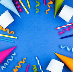 Party tools with cake, drinks and confetti on a blue background, top view, space for text. Background for a birthday greeting card