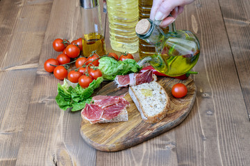 Sandwiches with jamon, olive oil dripping on the slice of bread and some vegetables on the wooden kitchen background. Healthy food for snack.