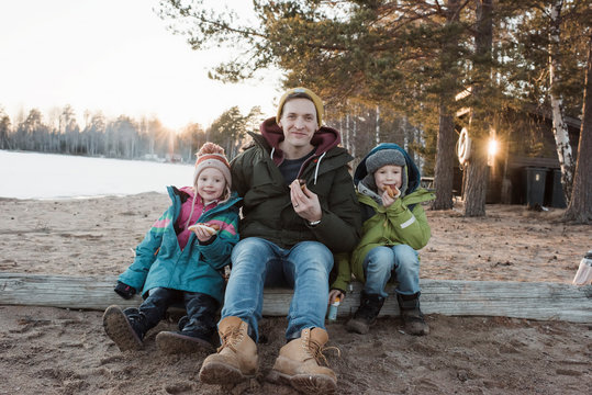 father and his kids eating hot dogs at the beach together in winter