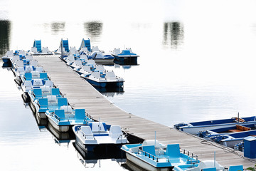 View of the pier, blue catamarans and boats standing in even rows on the lake. The concept of vacation, landscape, summer, entertainment.
