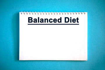 Balanced diet - text on a white notebook on a blue background