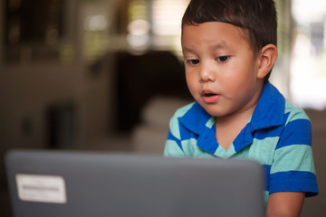 Young hispanic boy learning to pronounce words using a laptop and dedicated workspace at home.