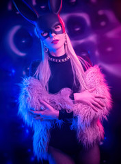 sexy girl in a bodysuit and fur coat with a rabbit mask in the neon light