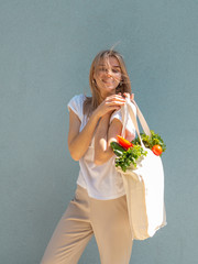 Smiling young woman holds a shopping bag with vegetables, products. Zero waste and vegan food...