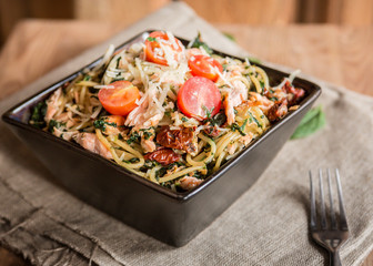 miska włoskiego makaronu spagetti z łososiem, pomidorkami koktajlowymi, suszonymi pomidorami i szpinakiem