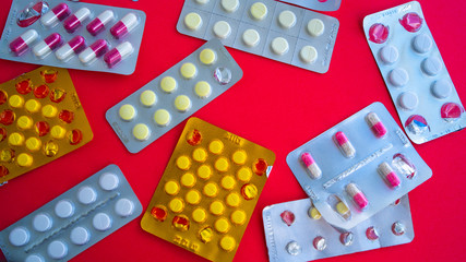 Close up of medical blister packs with tablets on red background. Packs with various tablets. Concept of threat of various diseases.