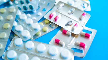 Close up of medical blister packs with tablets on blue background. Packs with various tablets. Concept of threat of various diseases.