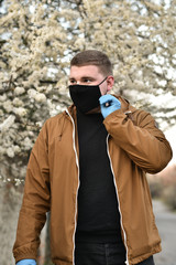 A guy in a medical mask and gloves on a background of flowers COVID-19, spring white Flowers blossomed on a branch, fruit tree
