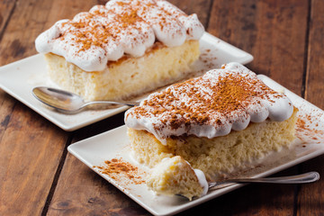 Two pieces of a delicious three milk cake dessert on a wooden background