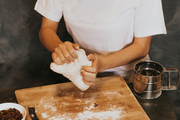 Young figured girl kneads the dough in a white T-shirt with long nails with natural manicure on a gray background. Lush dough with raisins during cooking