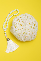 Muslim skullcap and white rosary on a yellow background