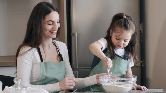 A pretty mother and daughter are making pastry for cookies. The kid and parent are celebrating Mother's day.