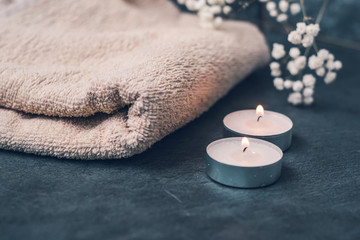 Light fluffy beige towels with spa paraphernalia, candles and flowers on a dark gray background