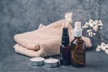 Cosmetic dark amber glass bottles on dark gray background. Closeup, copyspace. Dark glass containers with spa candles and flowers. Beauty blogging, salon treatment concept, minimalism packaging