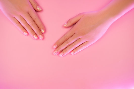 Stylish nude female manicure. Beautiful young woman's hands in trendy neon light on pink background. Beauty concept.