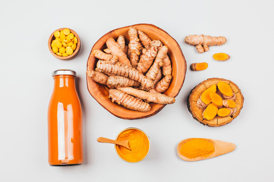 Turmeric in different states: fresh in bottle, pills, powder and cut plant on wooden tray, dry root in wooden bowl.