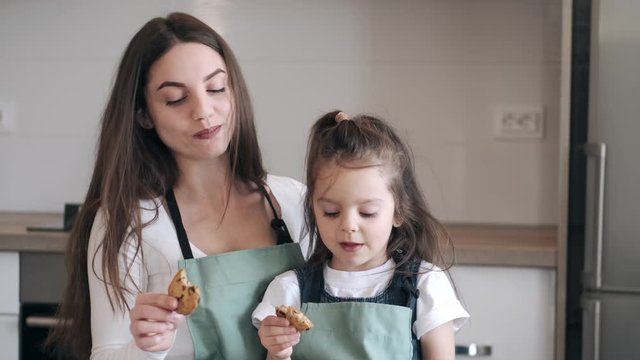 Mother and her kid dauhter are baking on Mother's day. They are eating cookies together. The parent and child are happy to spend time on such a holiday.