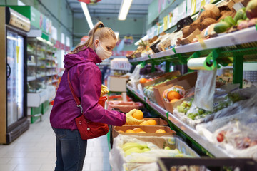 woman in protective mask and gloves buys fruit in a supermarket during an outbreak of coronavirus